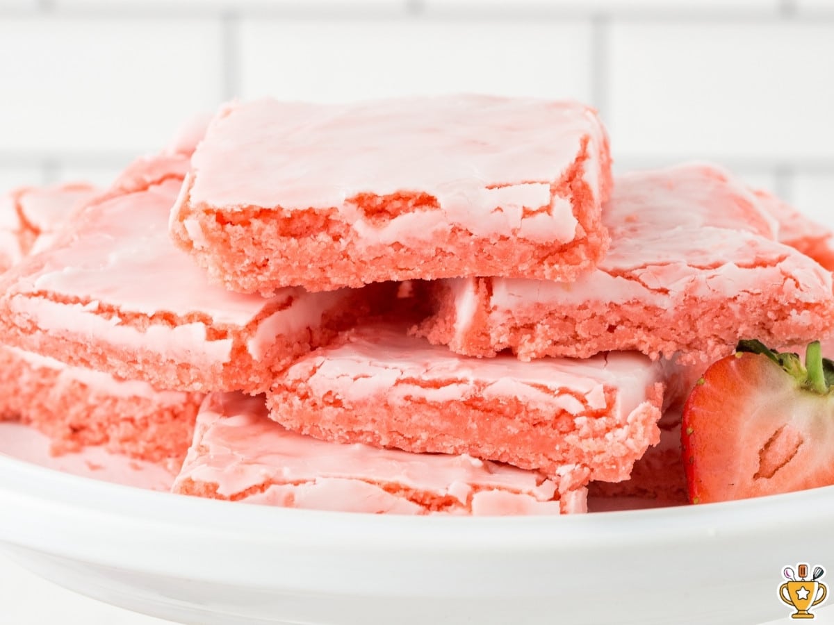 Stack of strawberry brownies with pale pink crackled icing on a white background
