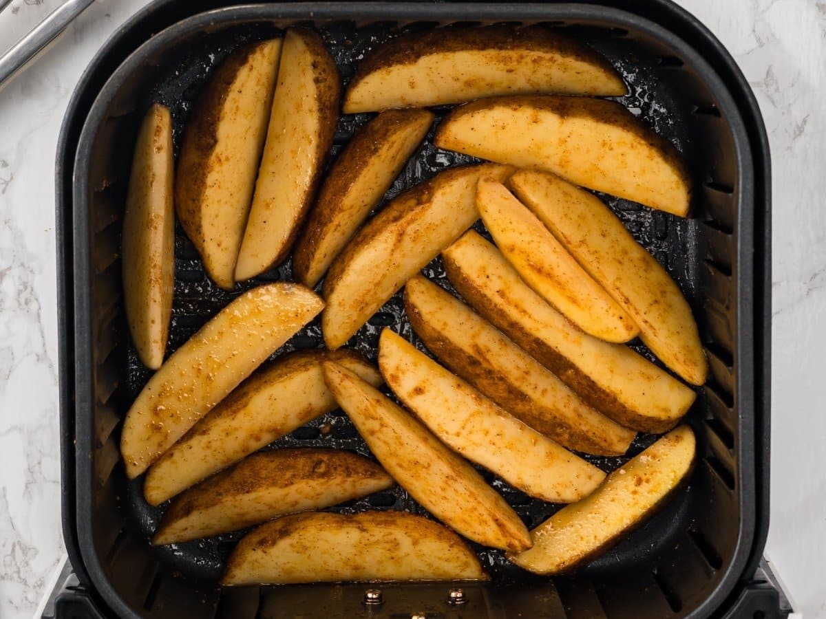 Seasoned potato wedges arranged in a single layer in an air fryer basket, ready to cook until crispy.
