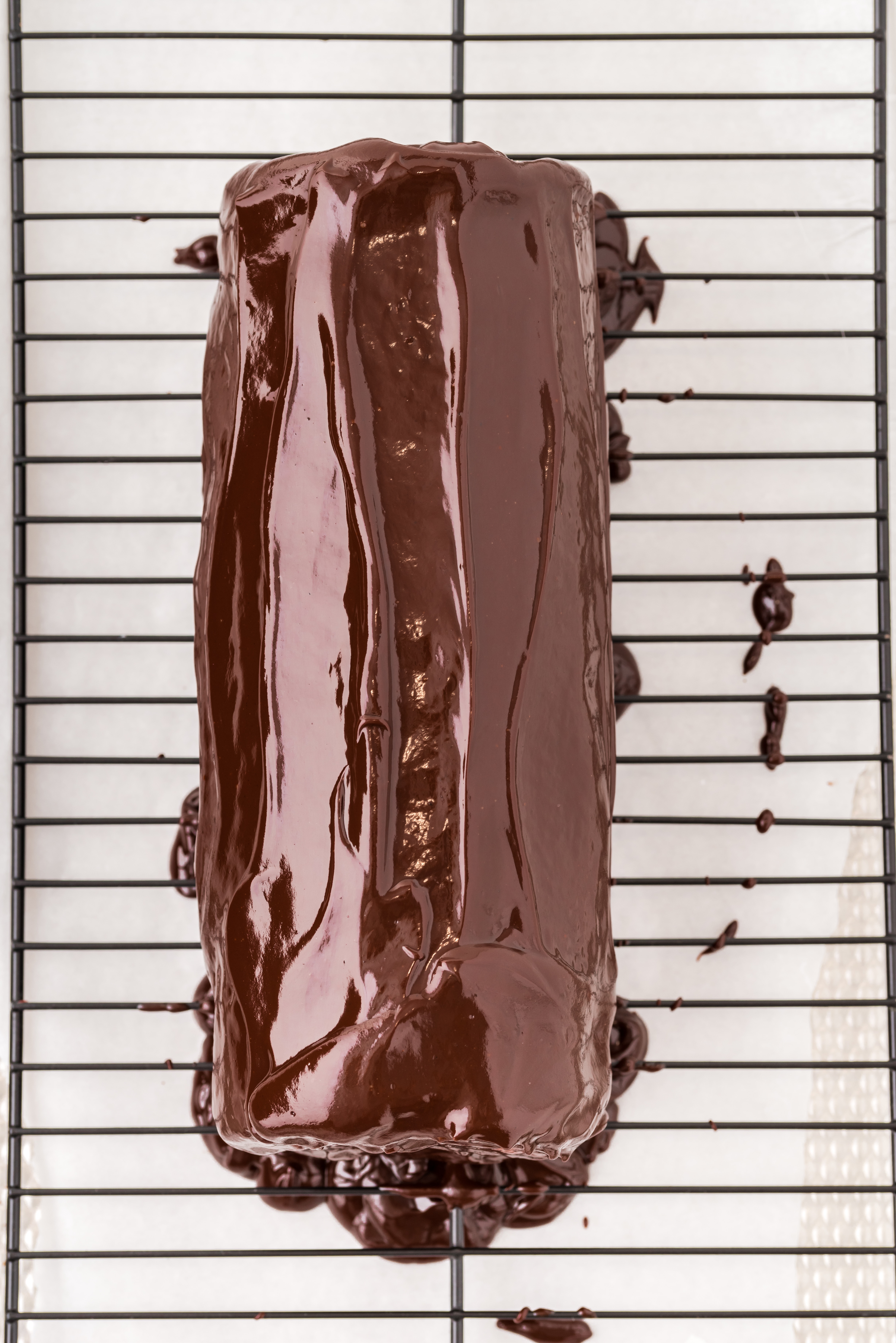 Top view of a chocolate Swiss roll cake coated in glossy chocolate ganache, set on a wire rack with excess ganache dripping below.