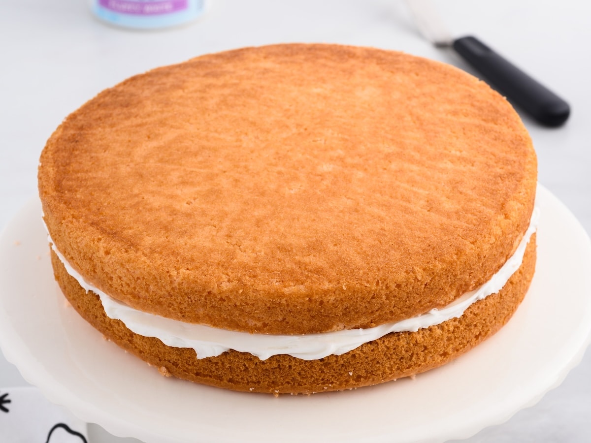 Two orange soda cakes stacked on a cake plate with frosting spread betwen the layers.