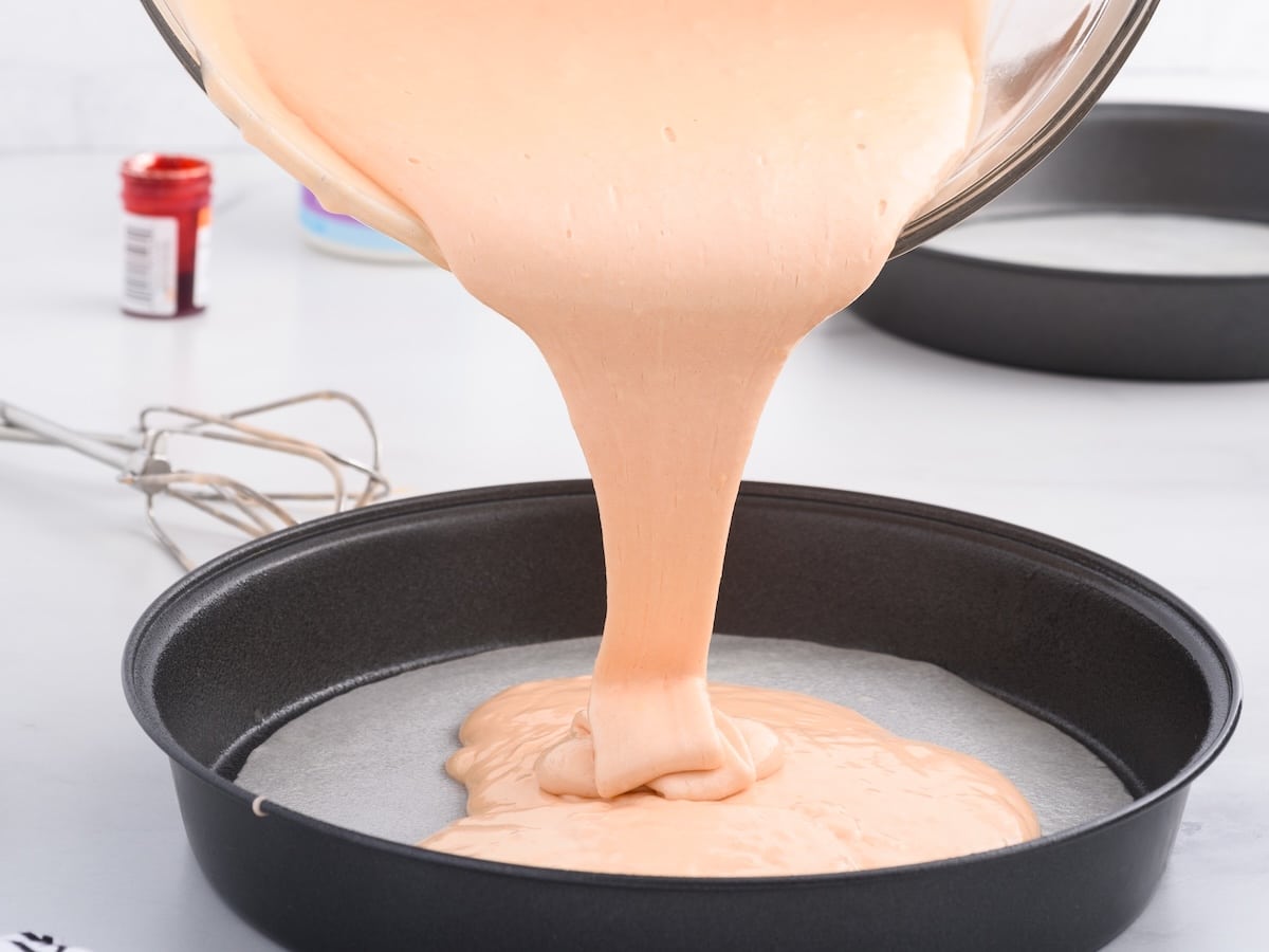 Orange soda cake batter being poured into a lined round cake pan, showing a smooth, slightly foamy, pourable consistency before baking.