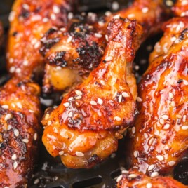 Close-up of air fryer honey garlic chicken wings in the air fryer basket with glossy honey garlic glaze, sesame seeds, and crispy caramelized skin