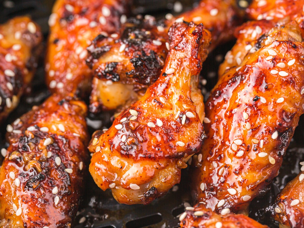 Close-up of air fryer honey garlic chicken wings in the air fryer basket with glossy honey garlic glaze, sesame seeds, and crispy caramelized skin