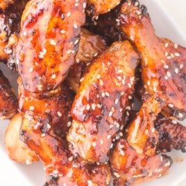 Air fryer honey garlic chicken wings piled on a white plate, coated in a shiny honey garlic glaze with sesame seeds and caramelized edges