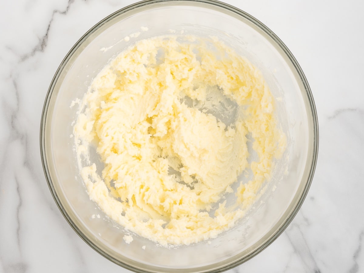 A glass bowl of creamed butter and sugar on a marble surface.