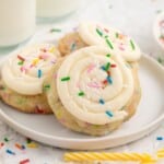 Close-up of Birthday Cake Cookies on a cooling rack with white frosting swirls, rainbow sprinkles, and colorful sprinkle-filled cookie dough.