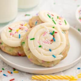 Close-up of Birthday Cake Cookies on a cooling rack with white frosting swirls, rainbow sprinkles, and colorful sprinkle-filled cookie dough.