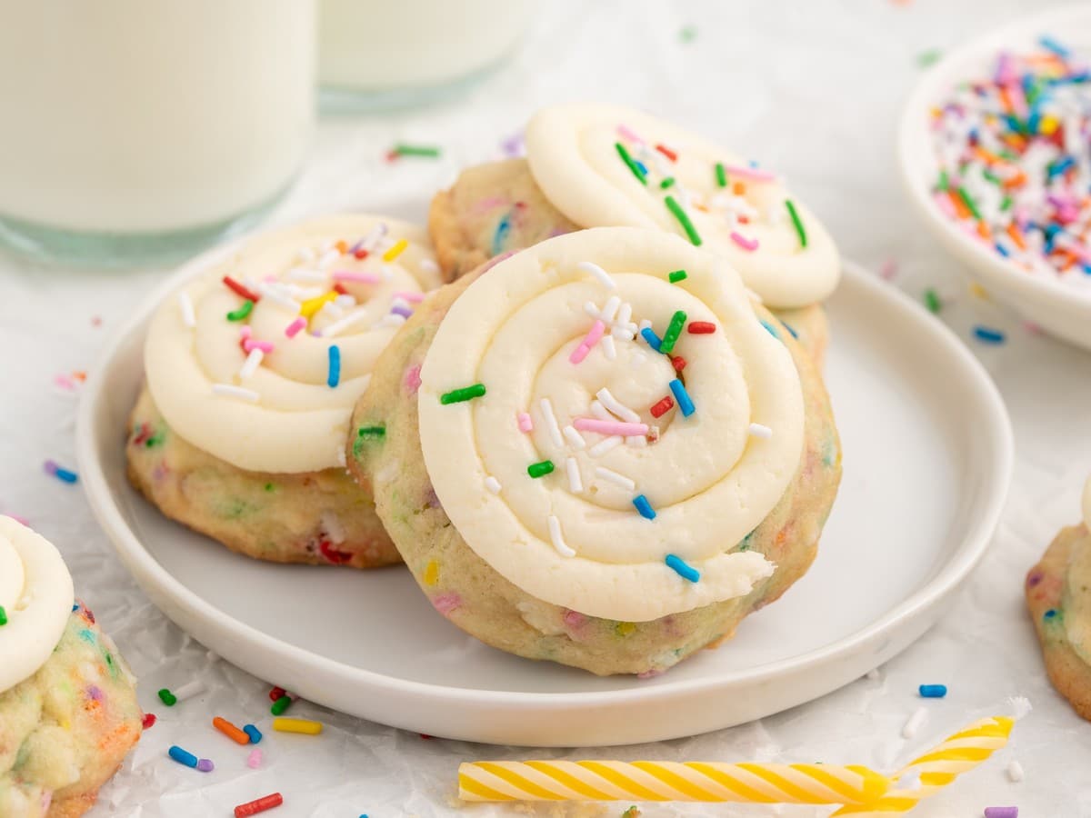 Close-up of Birthday Cake Cookies on a cooling rack with white frosting swirls, rainbow sprinkles, and colorful sprinkle-filled cookie dough.