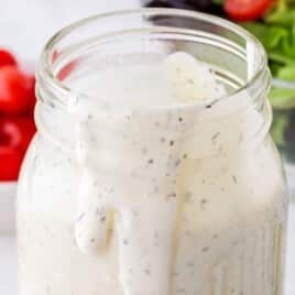 Creamy ranch dressing in a mason jar, thick and smooth with visible herb flecks, slowly dripping down the inside of the jar, with fresh vegetables blurred in the background.