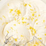 Creamy lemon cream cheese frosting in a glass bowl topped with fresh lemon zest next to a frosted cupcake, with text that reads makes a full 8 cups of frosting