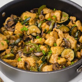 Panda Express mushroom chicken in a black skillet with chicken breast, mushrooms, zucchini, green peppers, sesame seeds, and chopped green onions in savory sauce