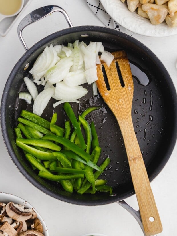 Onions and green pepper slices cooking in a large skillet.