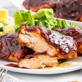 Featured image of Baked Barbecue Chicken Thighs with a thick BBQ glaze, tender sliced chicken, and crispy browned edges served on a white plate.