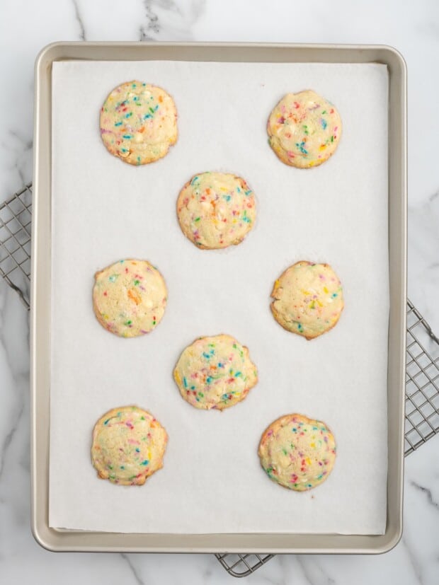 Freshly baked birthday cake cookies on a parchment-lined baking sheet, golden around the edges and soft in the center.