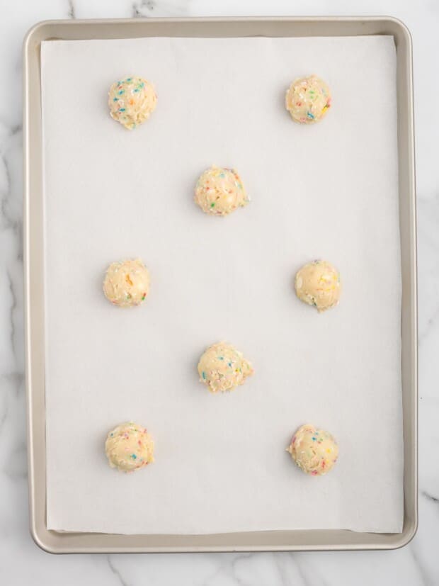 Birthday cake cookie dough balls spaced two inches apart on a parchment-lined baking sheet, ready to bake.