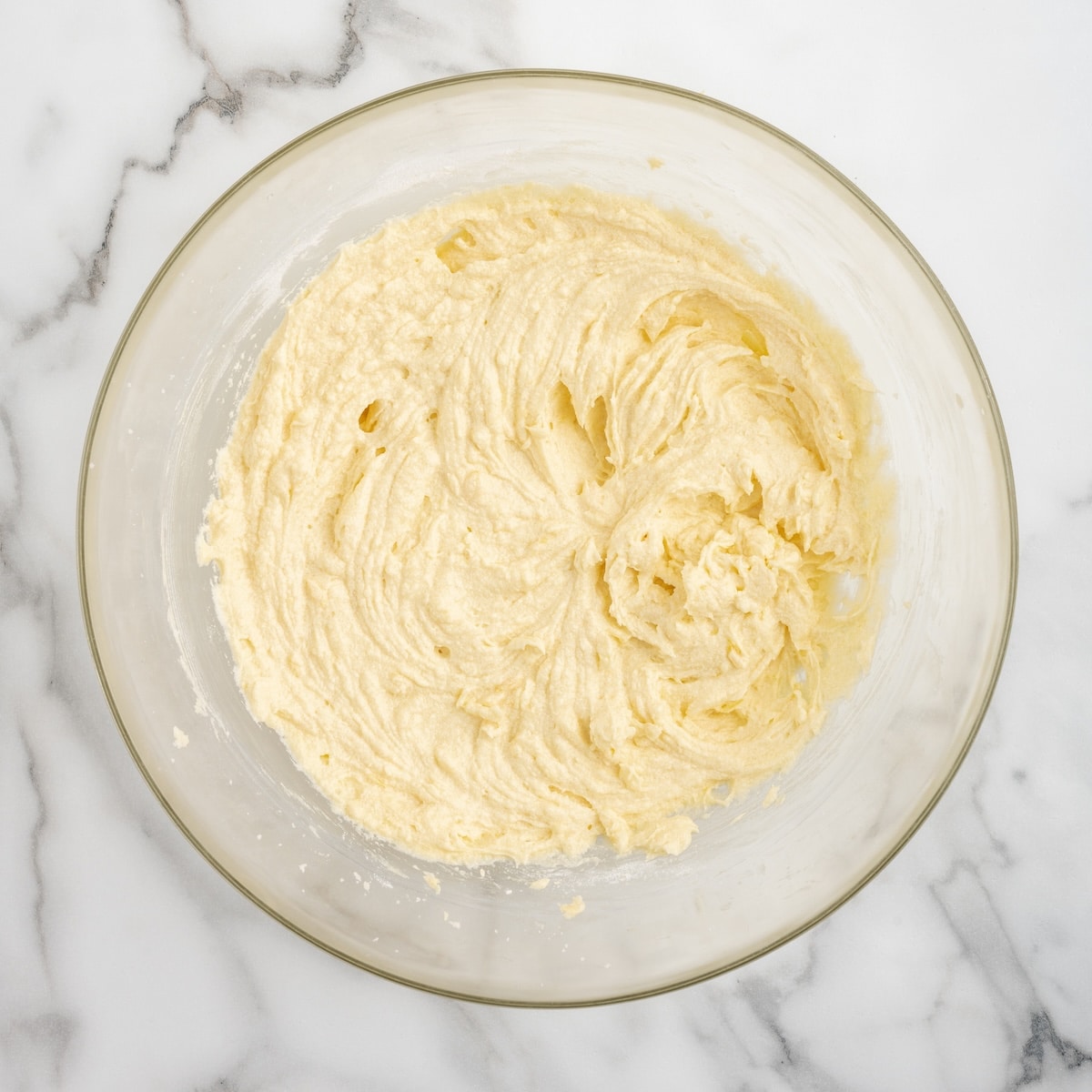 Lemon blondie batter in a glass bowl after eggs and lemon have been incorporated, showing a smooth, pale yellow, ribbony texture.