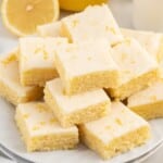 Lemon blondies cut into squares and arranged on parchment-lined wooden board with glossy lemon glaze and fresh lemon slices nearby