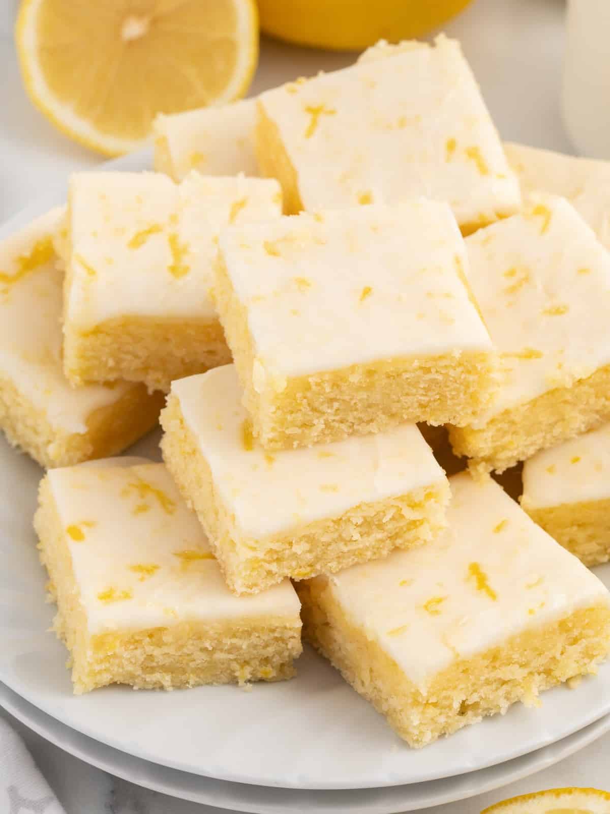 Overhead view of measured ingredients for lemon blondies on a marble surface, including butter, powdered sugar, eggs, baking powder, sugar, lemon juice, lemon zest, salt, and flour, each labeled with text