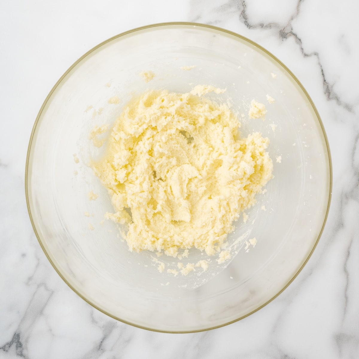 eamed butter and sugar in a glass bowl on a marble surface, showing a light and fluffy texture.