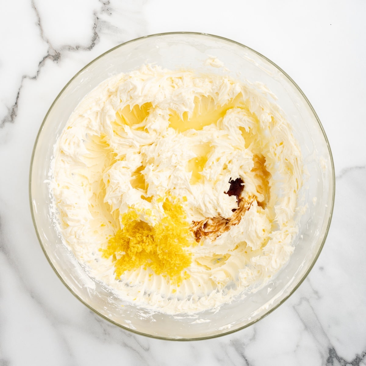 Lemon zest, lemon juice, and vanilla extract added to the whipped cream cheese and butter mixture in a glass bowl