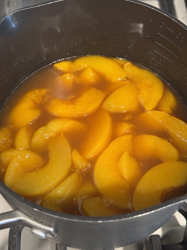 Peach slices simmering in syrup with cinnamon in a saucepan on the stove