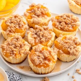 Mini peach cobbler cheesecakes on a plate topped with spiced peaches and crumble with syrup drizzle