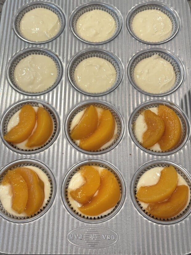 Peach slices placed on top of cheesecake batter in muffin pan before baking