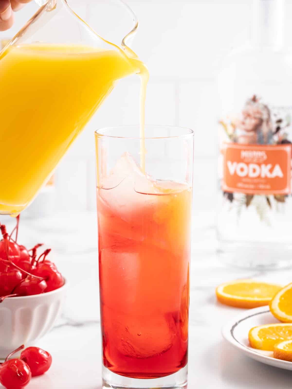 Orange juice being poured into a Sex on the Beach cocktail showing red layered base in a highball glass