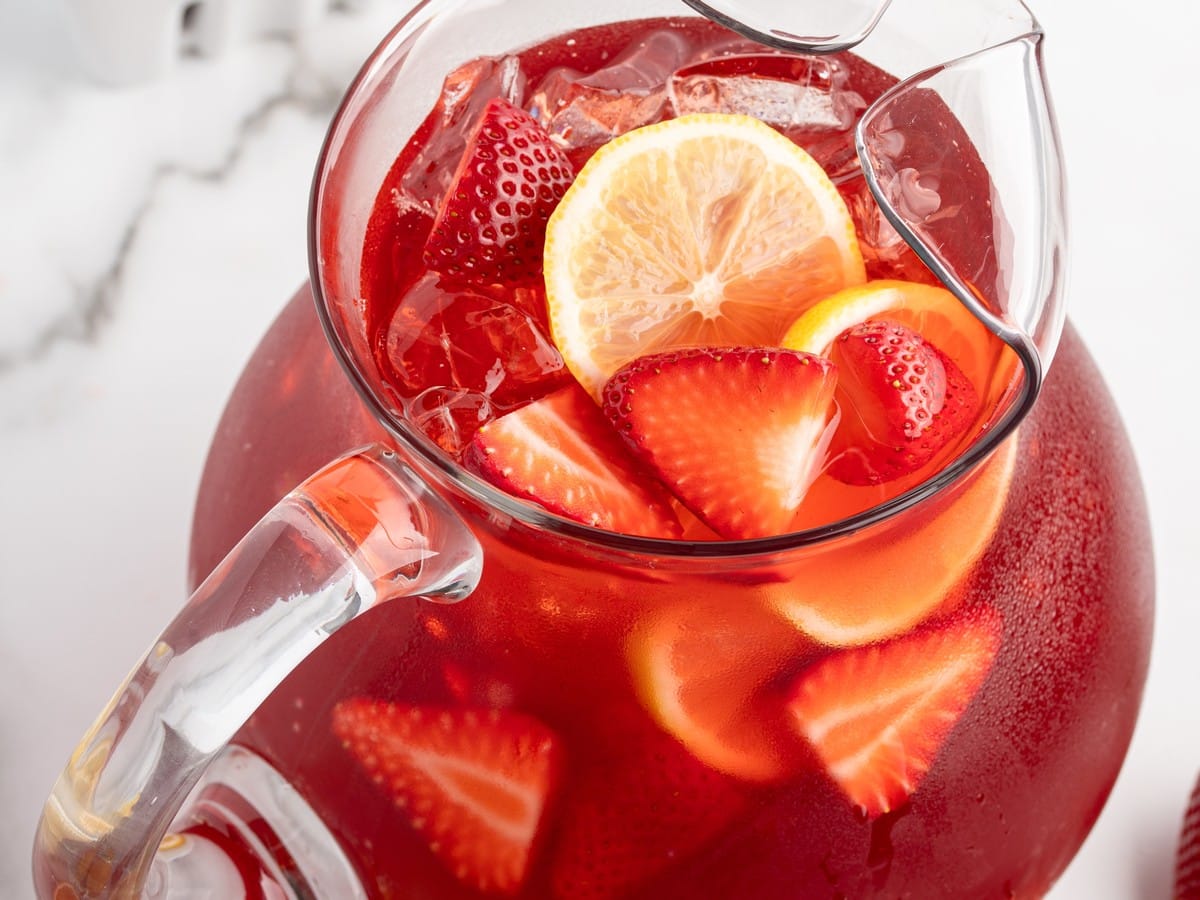 Pitcher of Southern Strawberry Sweet Tea with ice, sliced strawberries, and lemon rounds on a bright white countertop.