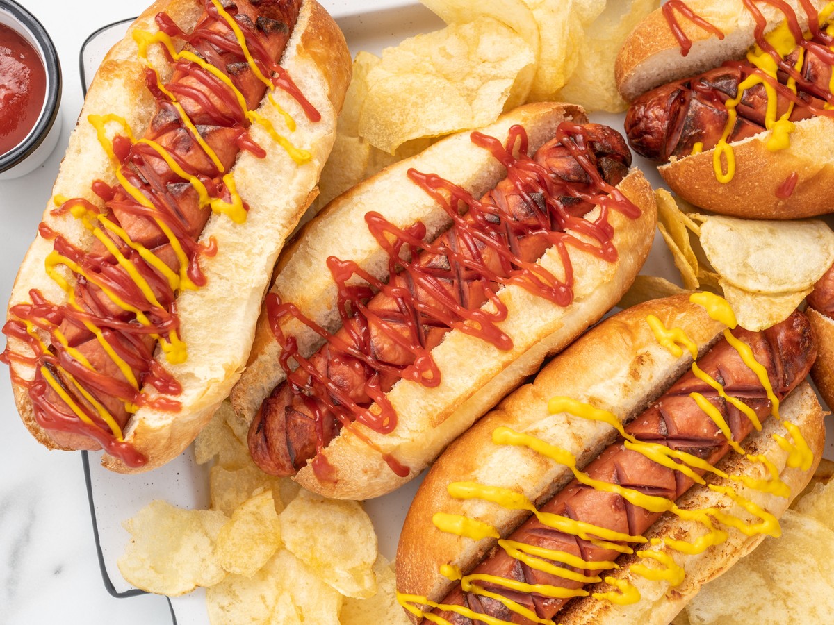 Close-up overhead image of air fryer hot dogs served in toasted buns with ketchup and mustard, arranged with potato chips on a serving tray for an easy air fryer hot dog meal.
