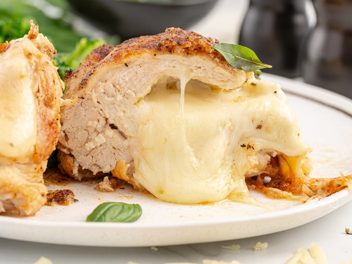 Close-up of sliced cheese stuffed chicken breast with tender white meat, gooey melted cheese filling, browned crust, and fresh basil.