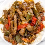 Close-up overhead photo of Crock Pot Pepper Steak served over white rice with tender beef strips, red and green bell peppers, onions, and rich brown sauce.