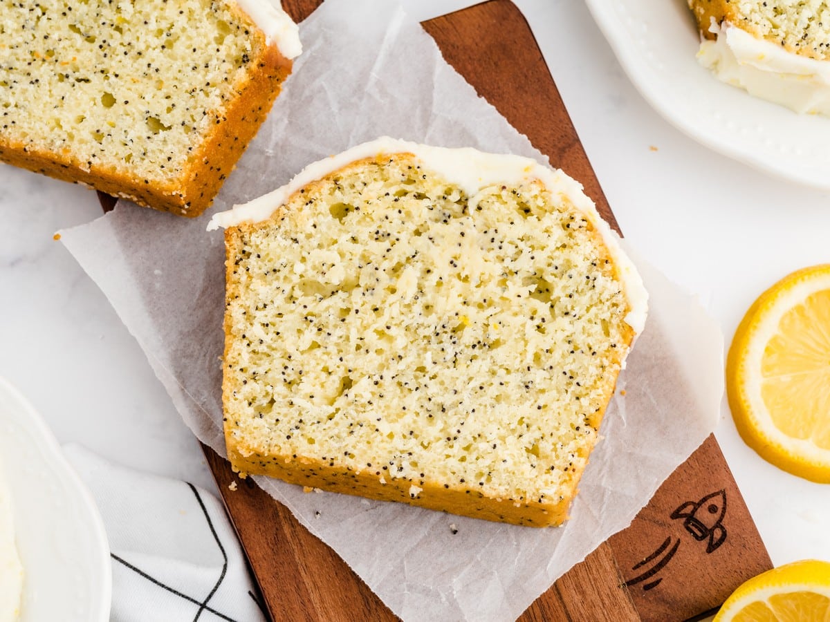 Single slice of lemon poppy seed bread on parchment paper showing the moist crumb, black poppy seeds, and lemon glaze.