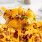 Close-up of Mississippi Mud Potatoes with melted cheddar cheese, bacon pieces, and green onions being lifted from the baking dish with a serving spoon.