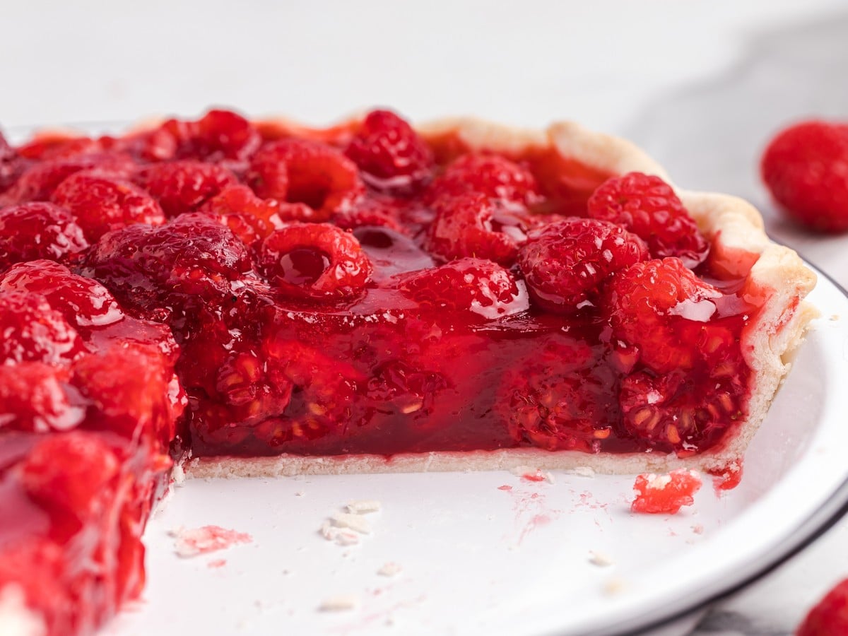Close-up of homemade raspberry pie with glossy raspberry filling packed with whole fresh raspberries in a flaky pie crust, showing the vibrant texture of the sliced dessert.