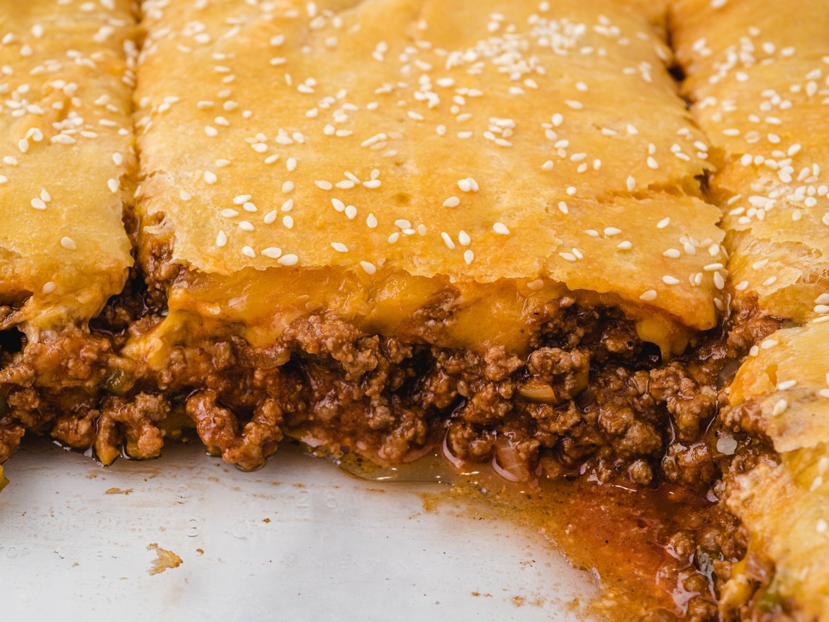 Detailed close-up of sloppy joe bake inside the baking dish, showing flaky golden crust with sesame seeds, melted cheese, and rich saucy ground beef filling.