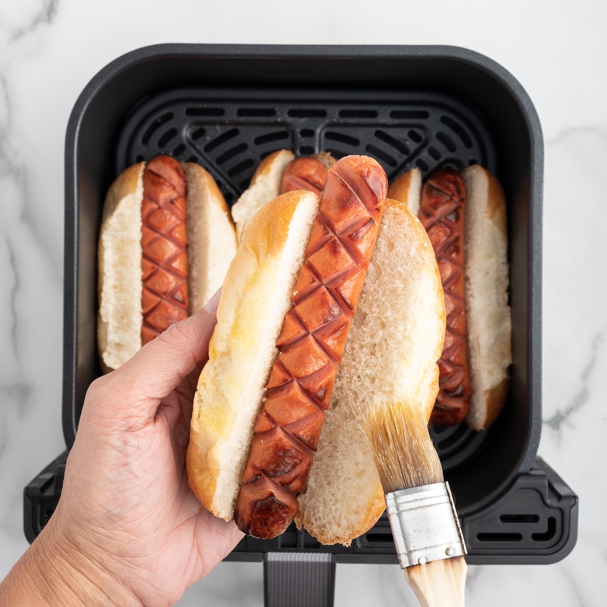 Brushing melted butter onto the edges of a hot dog bun before toasting in the air fryer.Brushing melted butter onto the edges of a hot dog bun before toasting in the air fryer.
