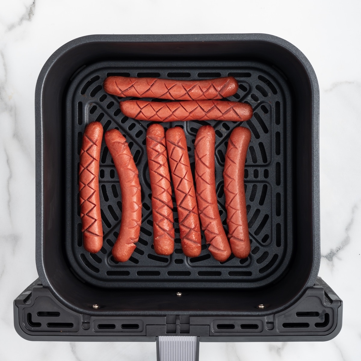 Eight diamond-scored Ball Park franks arranged in a single layer in an air fryer basket.