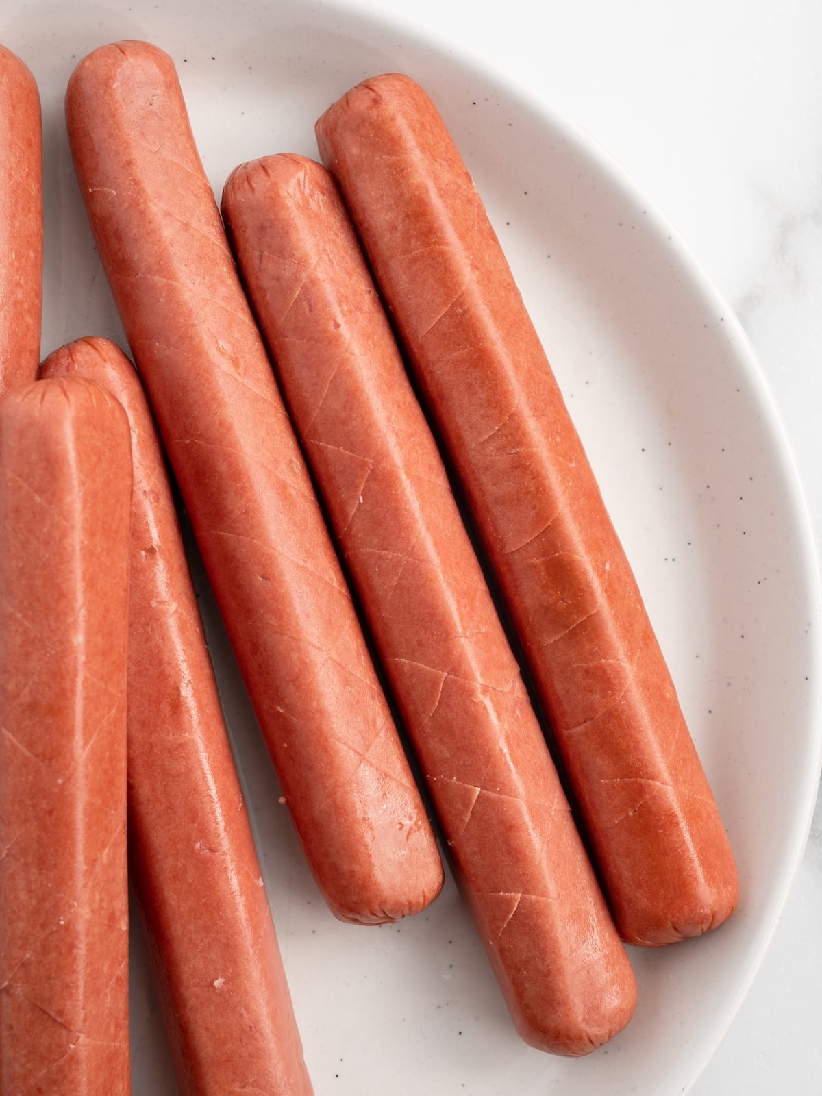 Diamond-scored Ball Park bun-length franks on a white plate, ready for the air fryer.