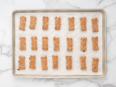 Bone-shaped bacon dog treat cutouts arranged on a parchment-lined baking sheet