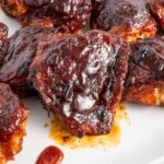 Close-up of baked BBQ chicken thighs on a white plate, coated in a thick, glossy barbecue glaze.