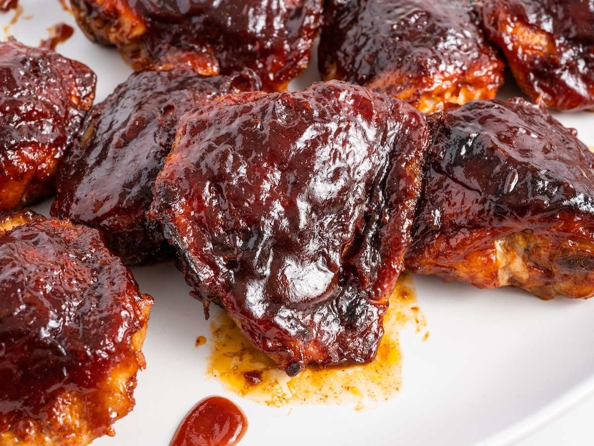 Close-up of baked BBQ chicken thighs on a white plate, coated in a thick, glossy barbecue glaze.