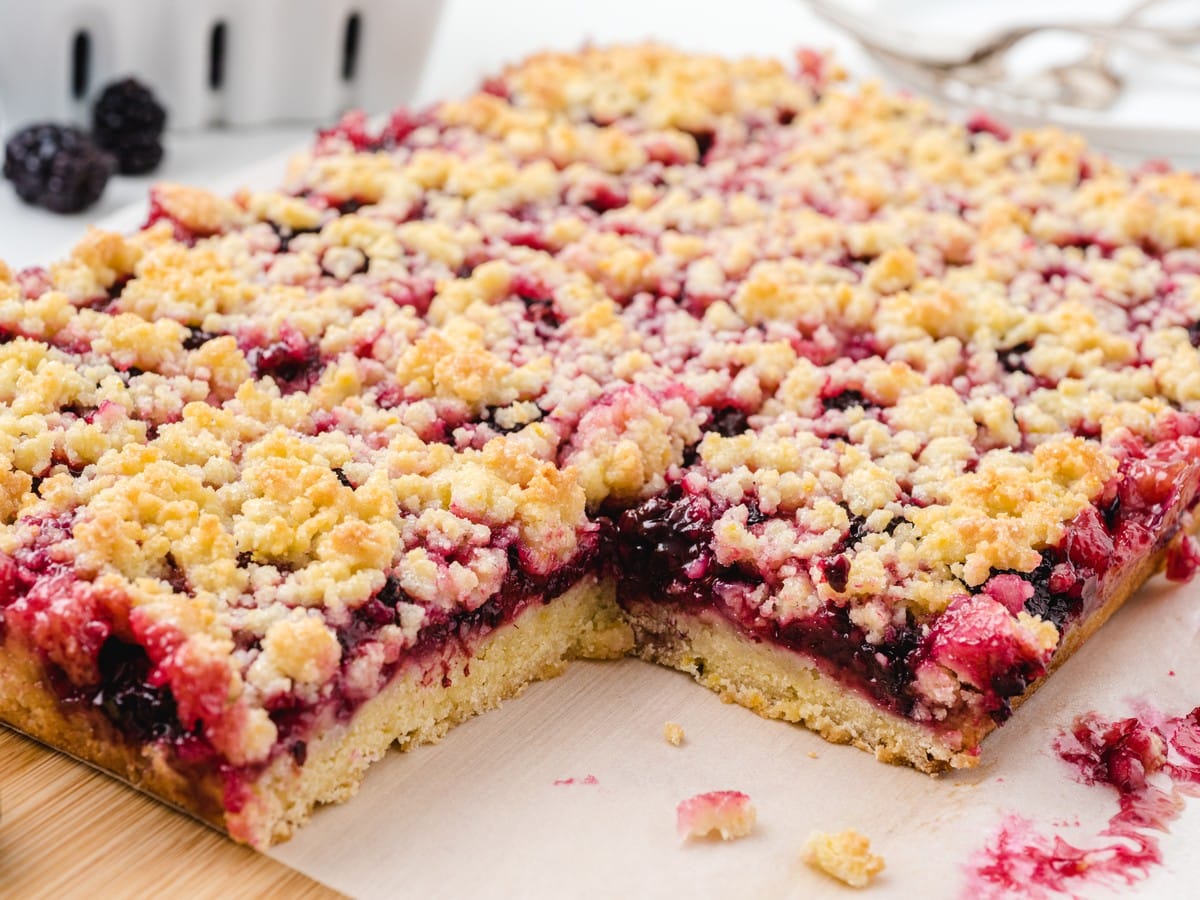 Blackberry bars on parchment paper with a golden crumb topping, thick blackberry filling, and buttery shortbread-style crust.