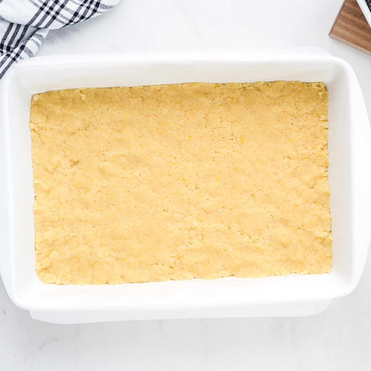 Pressed lemon pie bar crust in a white 9x13 baking dish