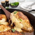Close-up of a golden brown cheese stuffed chicken breast in a cast iron skillet with melted cheese stretching from the center and fresh basil on top.