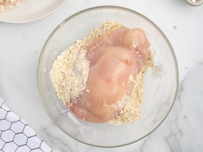 Raw stuffed chicken breast coated in seasoned breadcrumb mixture with toothpicks securing the filling inside.