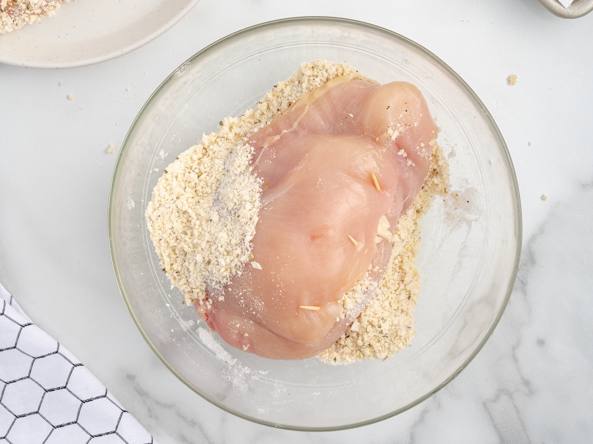 Raw stuffed chicken breast coated in seasoned breadcrumb mixture with toothpicks securing the filling inside.