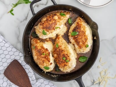 Cast iron skillet filled with golden brown cheese stuffed chicken breasts topped with fresh basil and melted cheese spilling from the center.