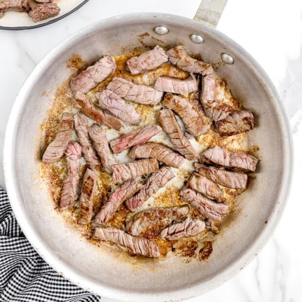 Beef strips browning in a skillet for crockpot pepper steak, showing browned edges with pink centers