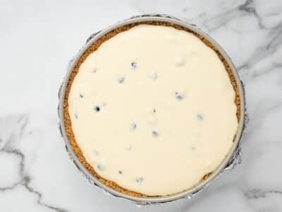 Lemon cheesecake batter with fresh blueberries folded in, spread evenly over the baked graham cracker crust in a foil-wrapped springform pan.